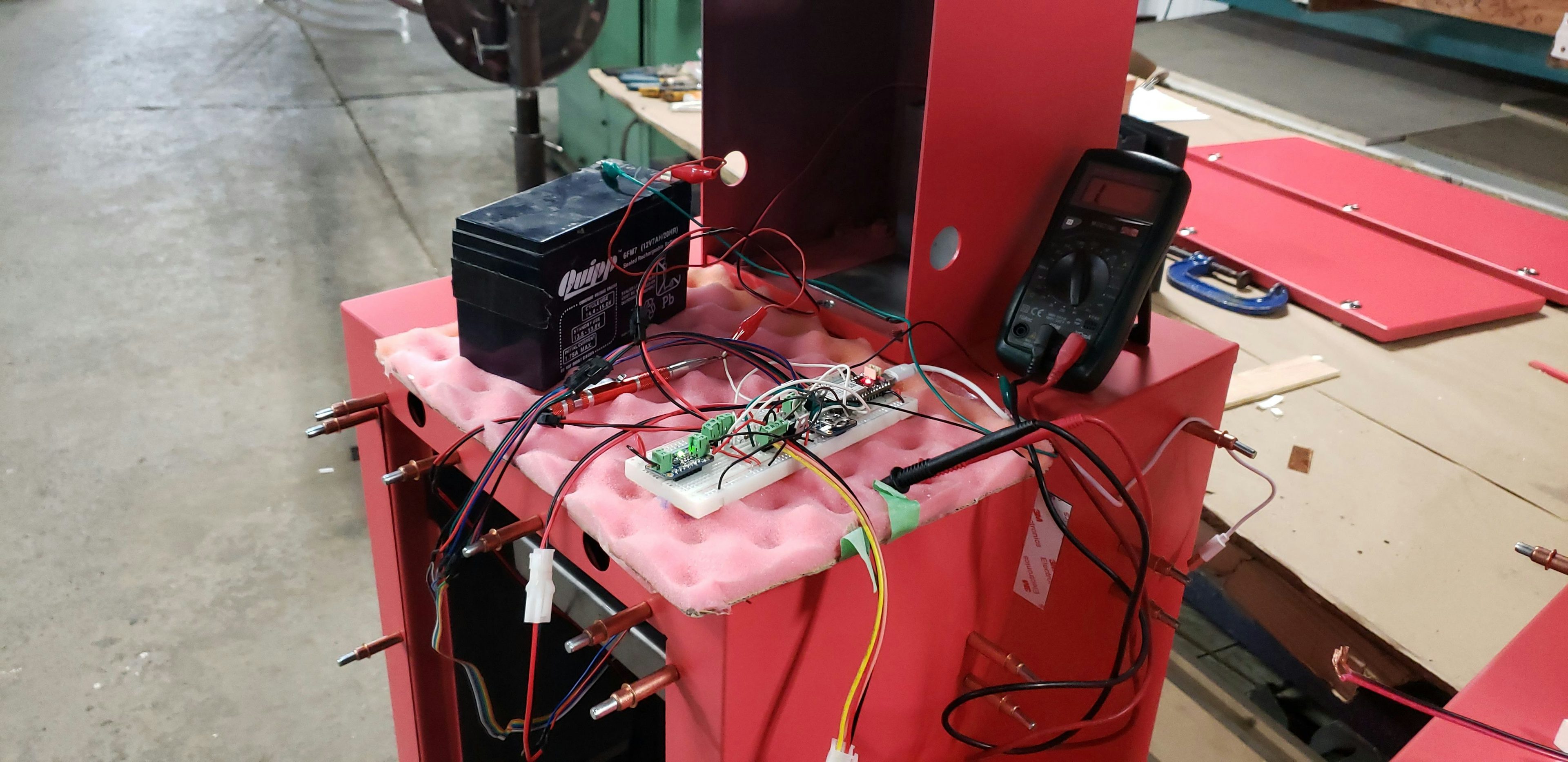 An SLA battery and circuits sit on top of a red newspaper box in a fabrication studio